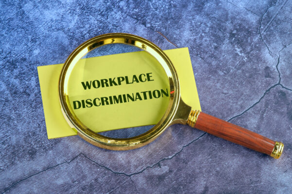 A concept image with letters WORKPLACE DISCRIMINATION appeared through a magnifying glass on yellow paper on an abstract background